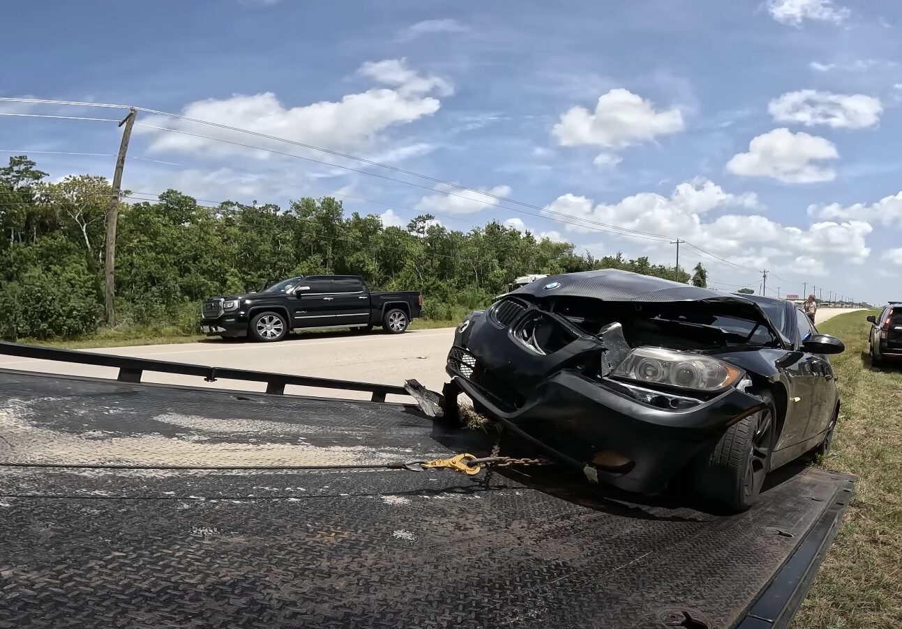 Damaged black sedan being loaded onto a flatbed tow truck after an accident